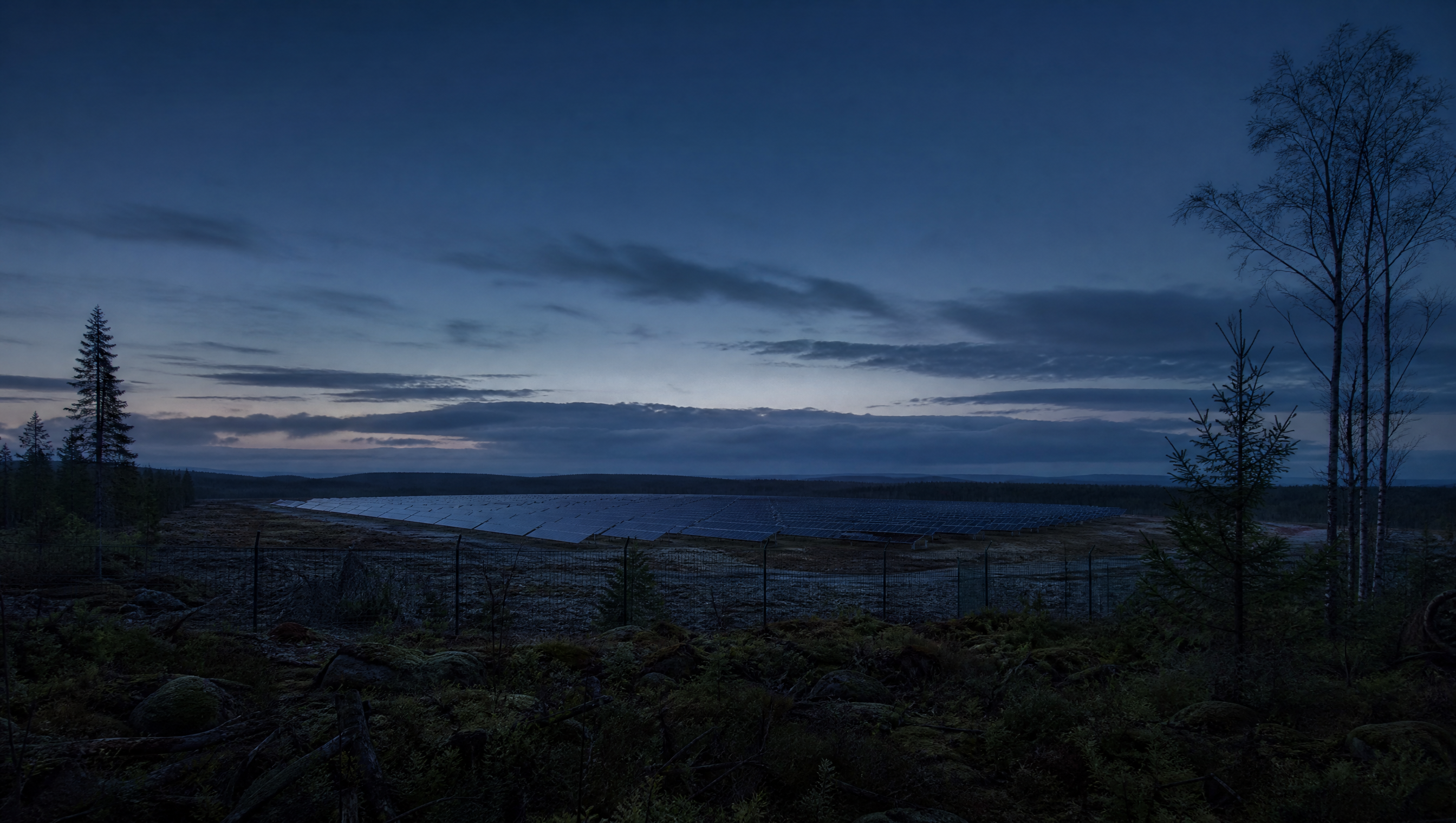 Utility-scale solar park at dusk in a Nordic landscape, perimeter fence visible in the foreground