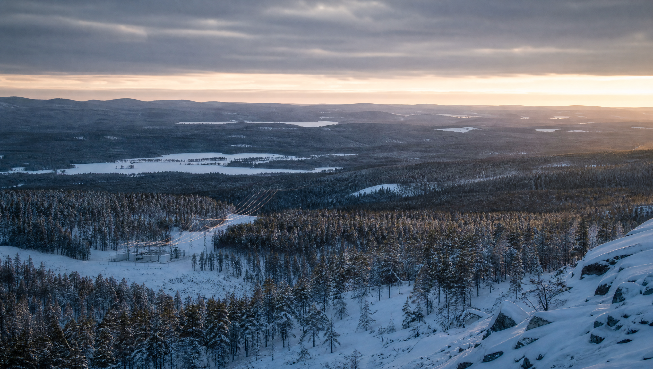 A Nordic winter landscape at dawn, transmission lines descending into a forested valley
